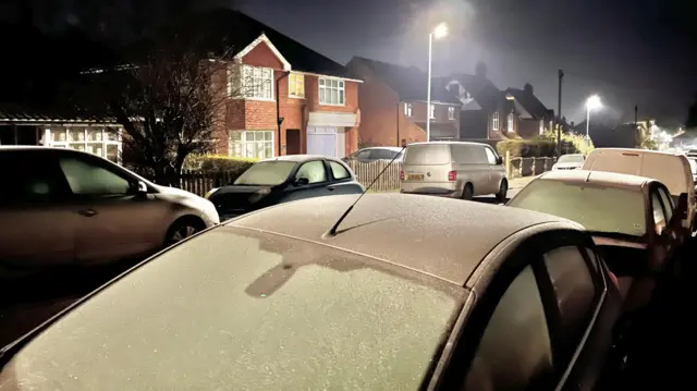 Parked cars covered in frost line the sides of a residential street