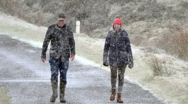 A pair in warm clothes walk side by side down a snow-covered mountain path in Wicklow, Ireland