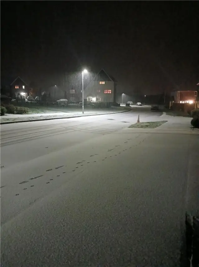 Snow is falling on a residential street.