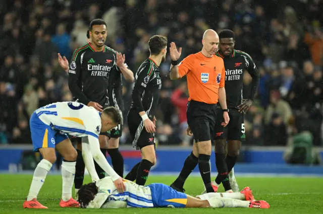 Arsenal players protest to the referee as Brighton players check on Pedro