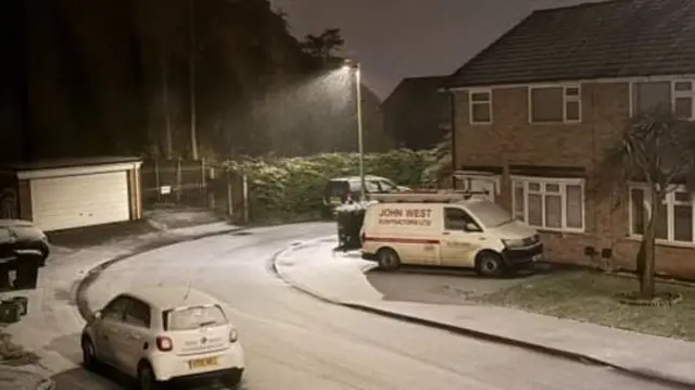 Snow in a street where you can see a car and a van parked