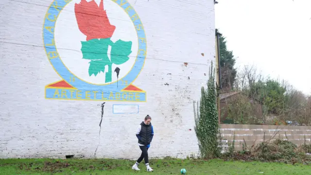 A fan kicks a ball around in front of a house with a Blackburn mural on the side