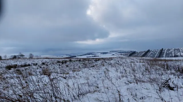 A landscape shot over snow covered ground. The sky is cloudy