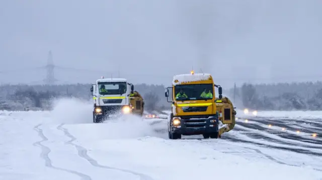 Two vehicles clearing the runway at Teesside Airport - the one at the front is yellow and the one behind is white