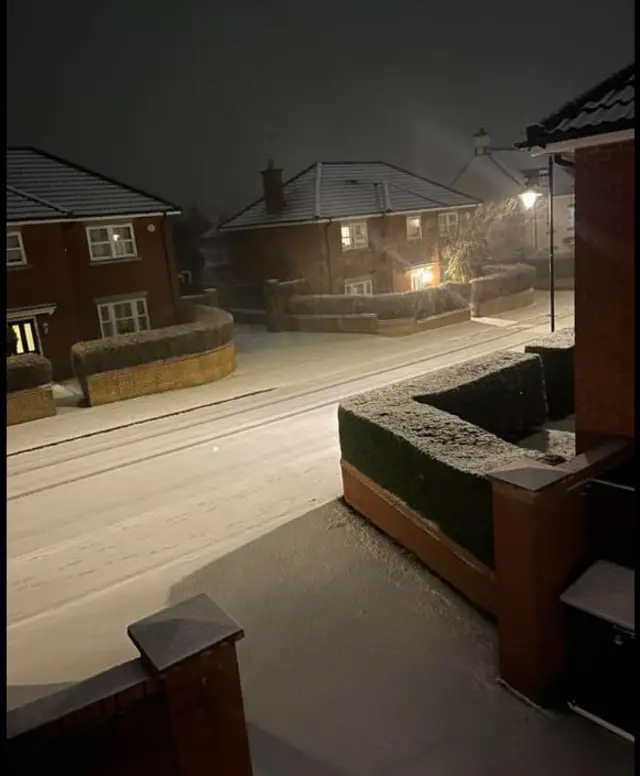 A street in Devizes with red-brick homes covered in a light dusting of snow, with streetlamps on