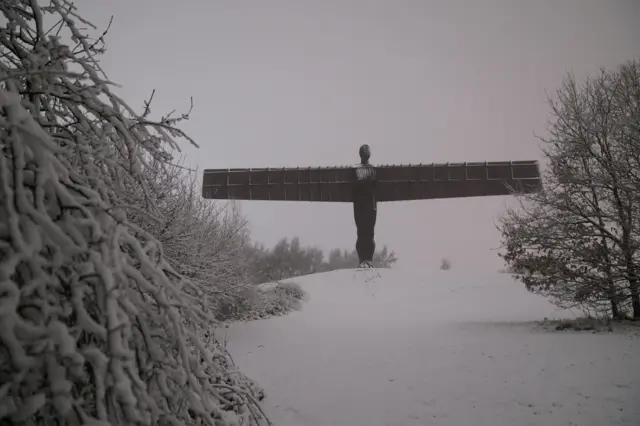 A large metal statue with outstretched wings surrounded by snow, looked at face on