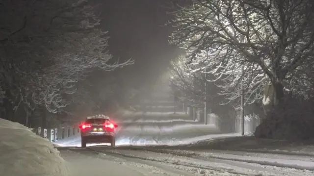 A car driving a long a snow covered road in the dark