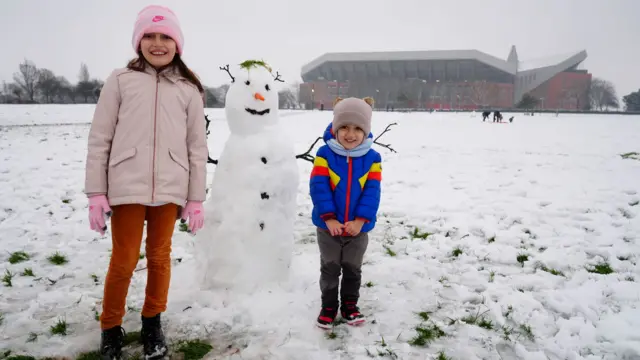 Two children stand beside a snowman