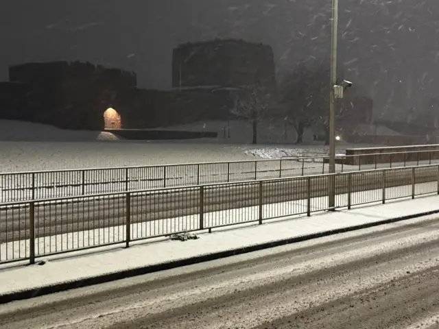 A dual carriageway in the foreground with Carlisle Castle in the background with snow falling