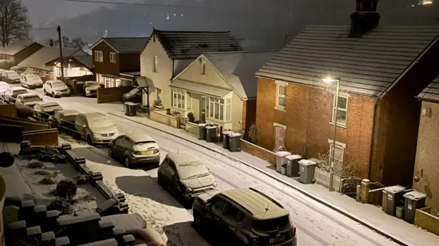 A look down on a residential street with cars parked along the side covered in snow