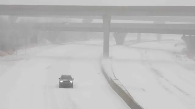 A single car drives along a snow-covered road