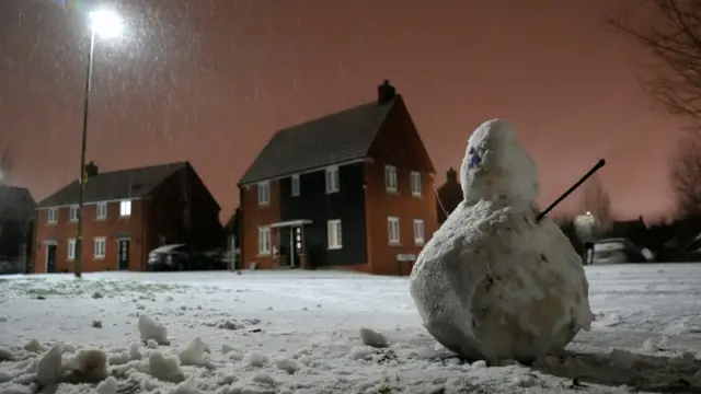 Snowman on the ground with houses in the background and snow on the road