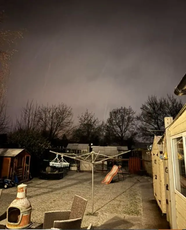 A garden in Street, Somerset with a light dusting of snow. In the frame you can see a washing line, slide, garden shed and chairs covered in snow