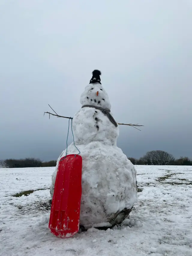 A large snowman with a red sledge propped up against it