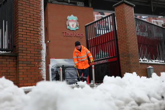 A steward clears snow outside the Kop at Anfield