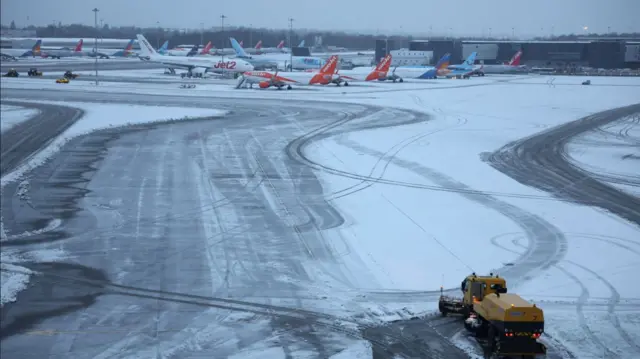 A snow plough waits to help clear snow from around aircraft after overnight snowfall caused the temporary closure of Manchester Airport in Manchester.