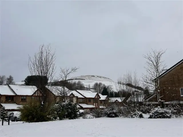 A snowy scene in Helmshore, Lancashire shows a field covered in snow, with Musbury Tor in the background