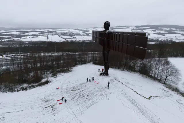 People sledge at the feet of the Angel of the North in Gateshead