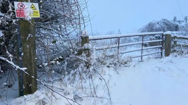 Corner of a snow covered field with a five barred gate on which snow is lying