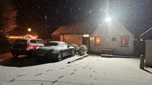 A house and two cars are covered in snow