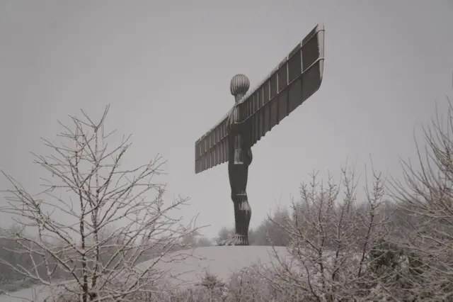 A side view of a large metal figure with outstretched wings surrounded by snow