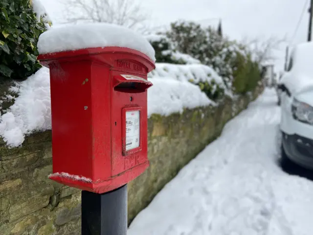 A red post box on a pole and covered in snow