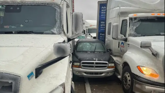 Black car sandwiched between two larger white trucks, covered in ice