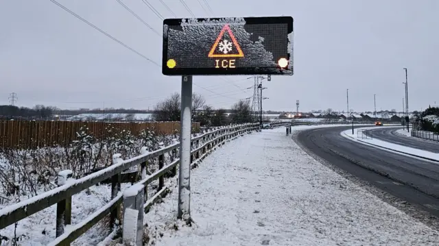 A large electronic road sign that says "ice" on it, surrounded by snow