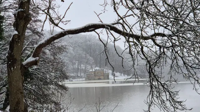 A castellated building in the distance seen through snowy trees and beyond a lake