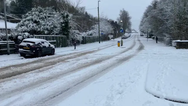 A car drives down a snow covered road.