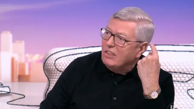 Alan Johnson in black shirt with raised pointer finger of left hand