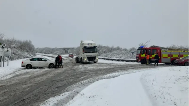 Fire truck on snowy road supporting white car and lorry getting stuck because of the bad weather