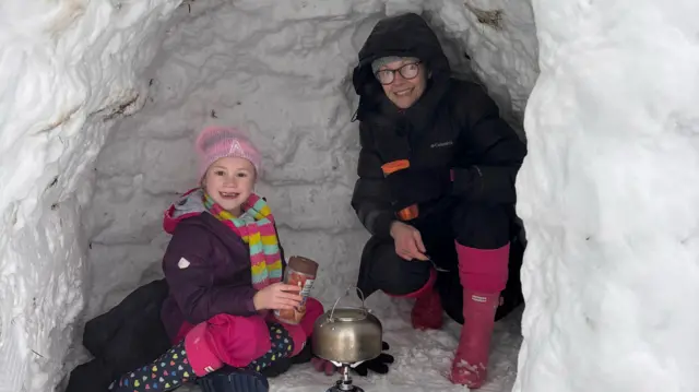 Annabelle and Lauren crouch in their igloo over a portable stove and kettle while making hot chocolate.