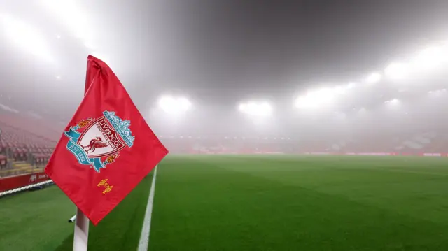 A Liverpool FC flag in the corner of an image of the Anfield Stadium