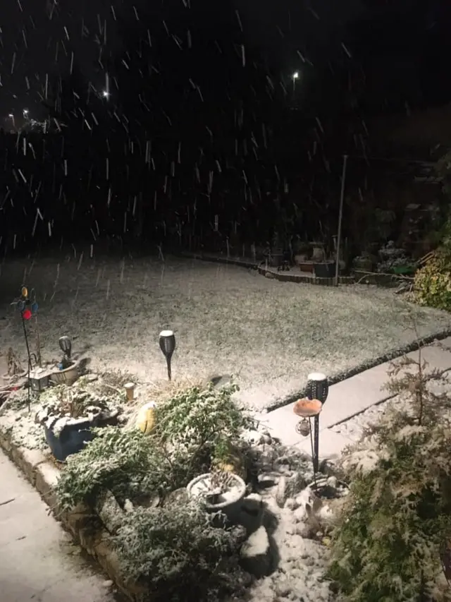 A garden in Kingswood, Bristol, with plant pots and a patio covered in snow. Snow is also falling