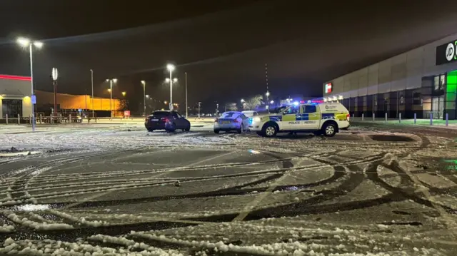 Police vehicles park next to two cars on icy ground