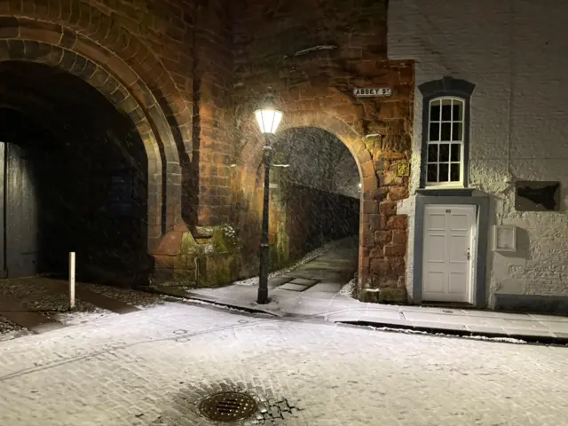 An archway on Abbey Street in Carlisle. A street light illuminates the snow falling on the ground