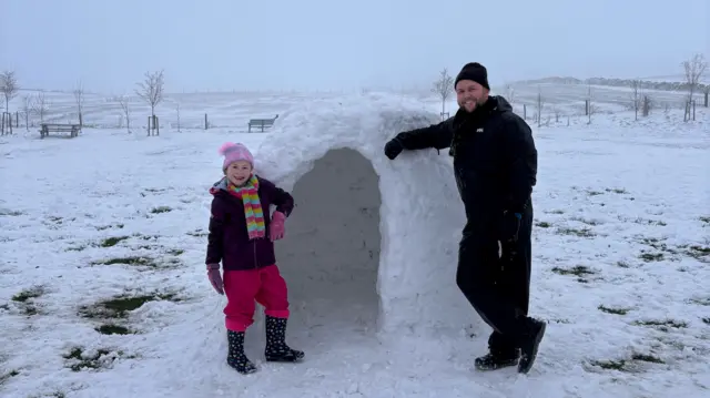 Annabelle and Kieran stand outside the entrance to their igloo.