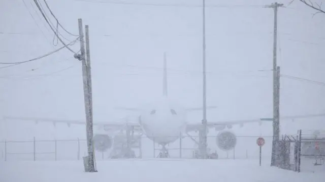 From a further angle, the FedEx plane is barely visible against a backdrop of white, heavy snow