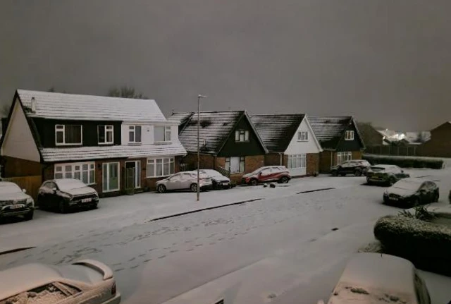 Snow on a sub-urban road with cars covered