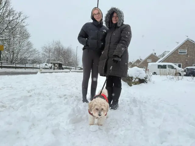 Two women in the snow walking a small dog