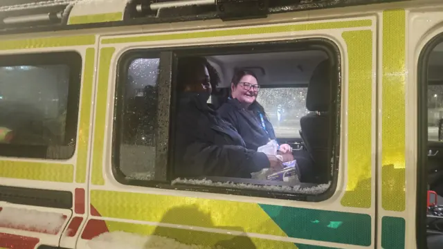 Two women in navy coats looking out of an emergency 4x4 vehicle window. They are smiling