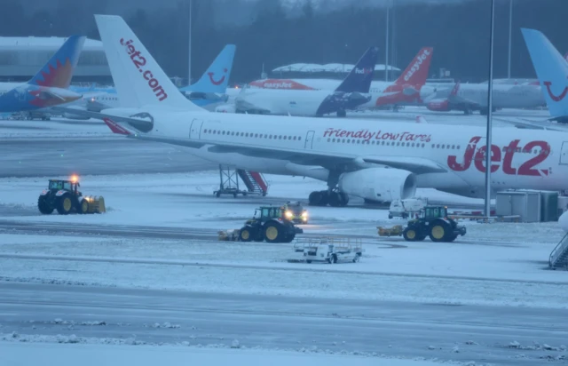 Staff use tractors to help clear snow from around aircraft after overnight snowfall caused the temporary closure of Manchester Airport