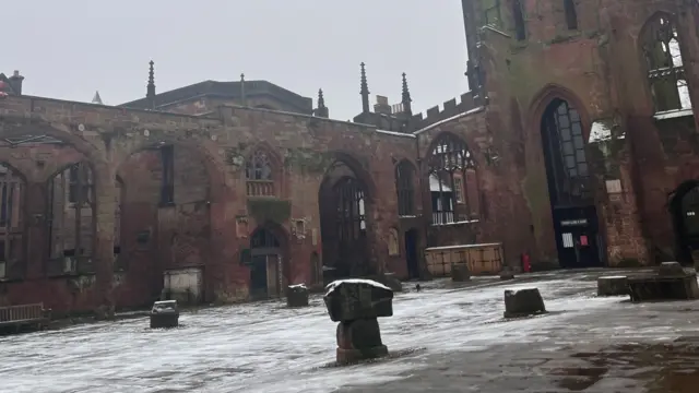 The inside of Coventry's ruined Cathedral, lightly covered in snow. The remains of ruined columns dot a courtyard that was once the church interior.