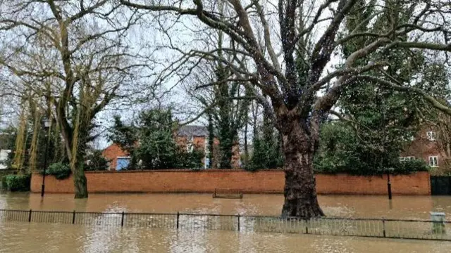 High flood water covering a road, a half-submerged fence and a bench half under water