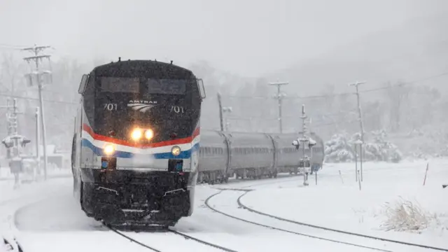 An Amtrak train during a storm in Hudson, with snow on and around the tracks and trees in the background