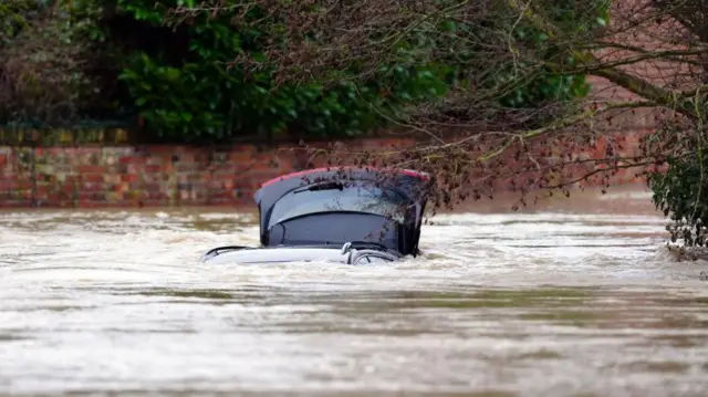 A car almost fully submerged. You can see its roof and boot open