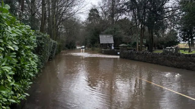 A car approaches a flooded country lane in Swithland