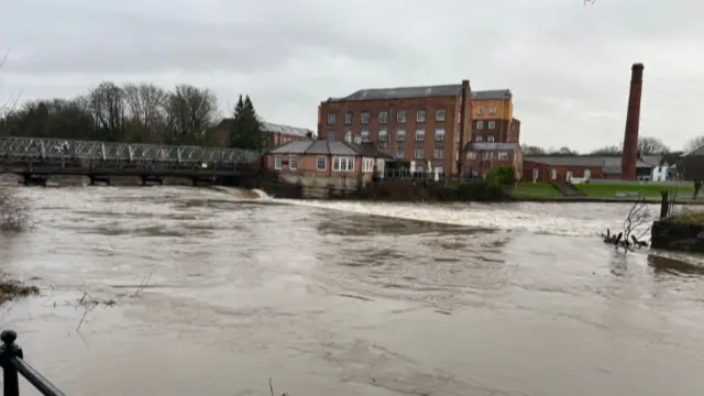 A surging river outside a Victorian industrial building