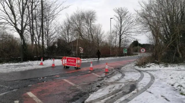 Traffic cones and a sign blocking a snowy road